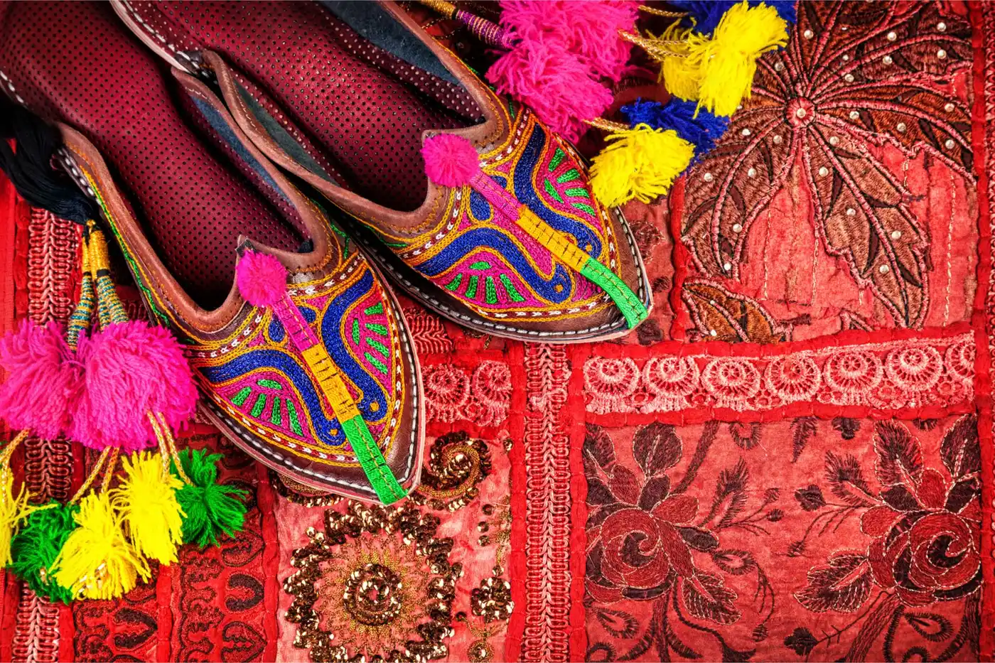 Colorful ethnic shoes and camel decorations on red Rajasthan cushion cover on flea market in India Colorful ethnic shoes and camel decorations on red Rajasthan cushion cover on flea market in India